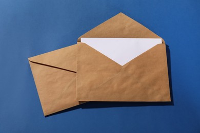 Photo of Kraft paper envelopes with letter on blue background, top view. Mockup for design