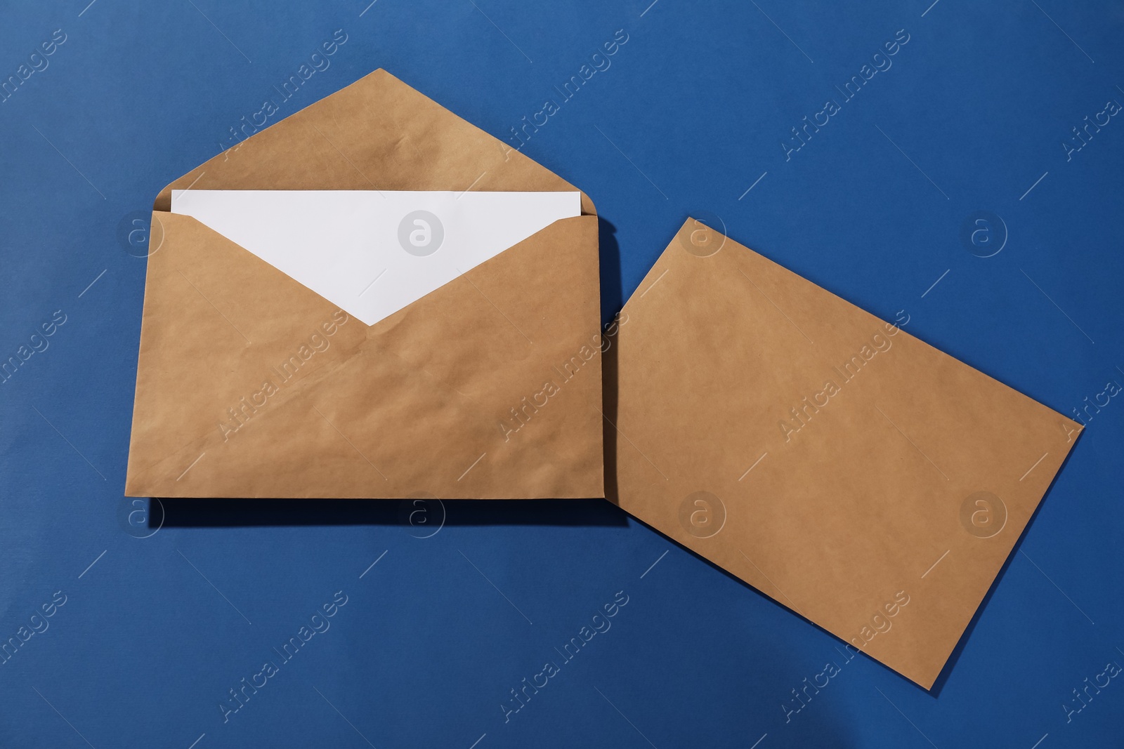 Photo of Kraft paper envelopes with letter on blue background, top view. Mockup for design