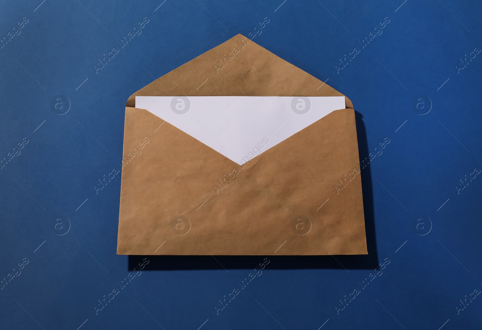 Photo of Kraft paper envelope with letter on blue background, above view. Mockup for design