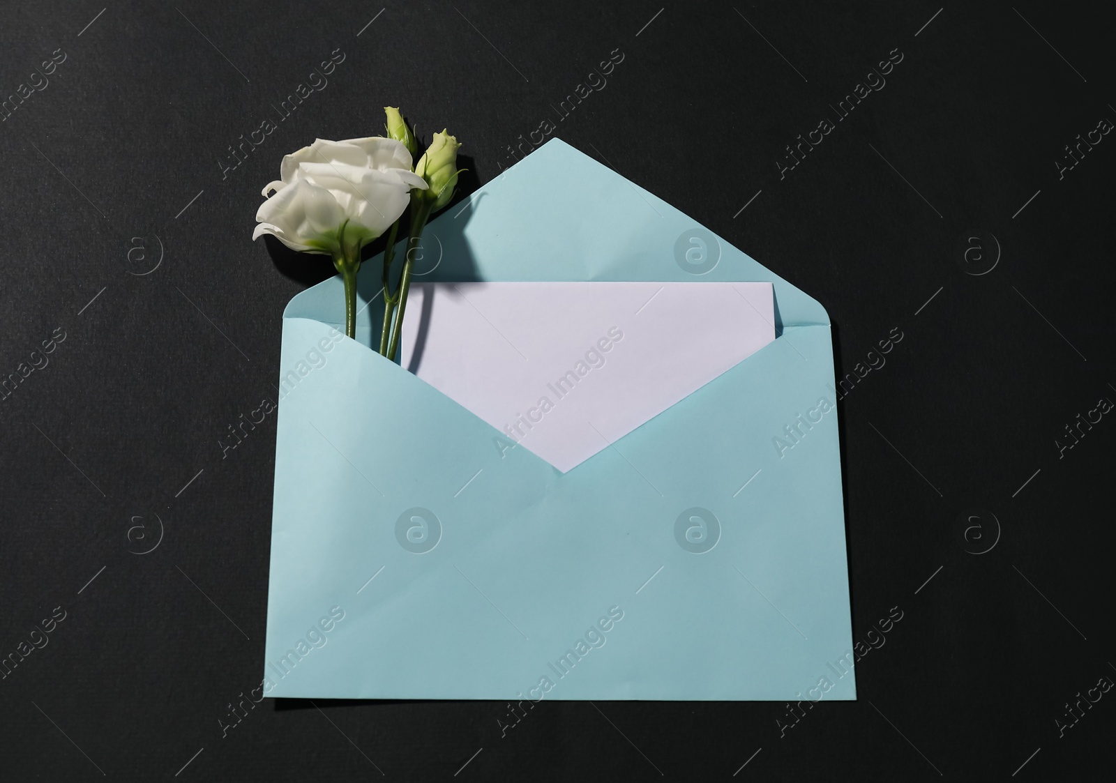 Photo of Paper envelope with letter and flowers on black background, top view. Mockup for design