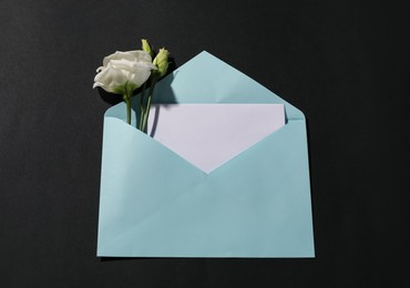 Paper envelope with letter and flowers on black background, top view. Mockup for design