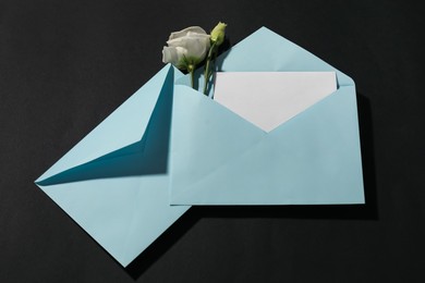 Photo of Paper envelopes with letter and flowers on black background, flat lay. Mockup for design