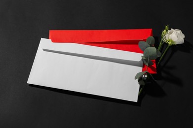 Photo of Paper envelopes, flower and eucalyptus branch on black background, above view. Mockup for design