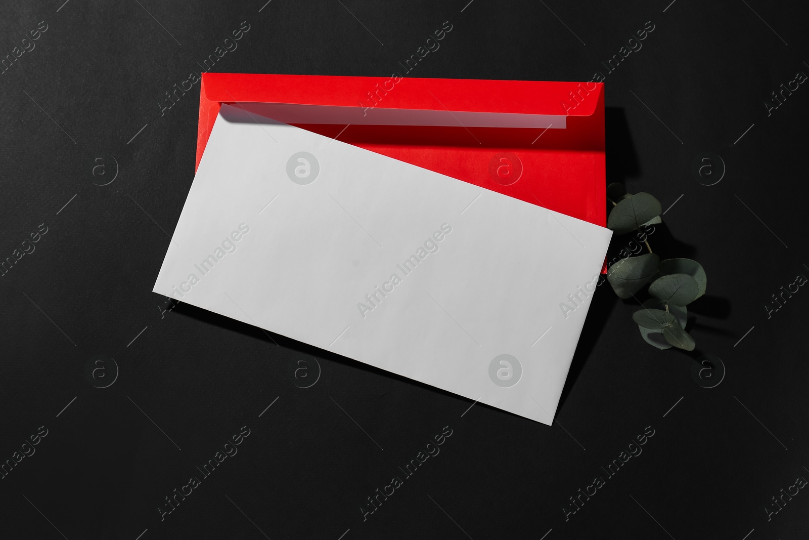 Photo of Paper envelopes and eucalyptus branch on black background, top view. Mockup for design