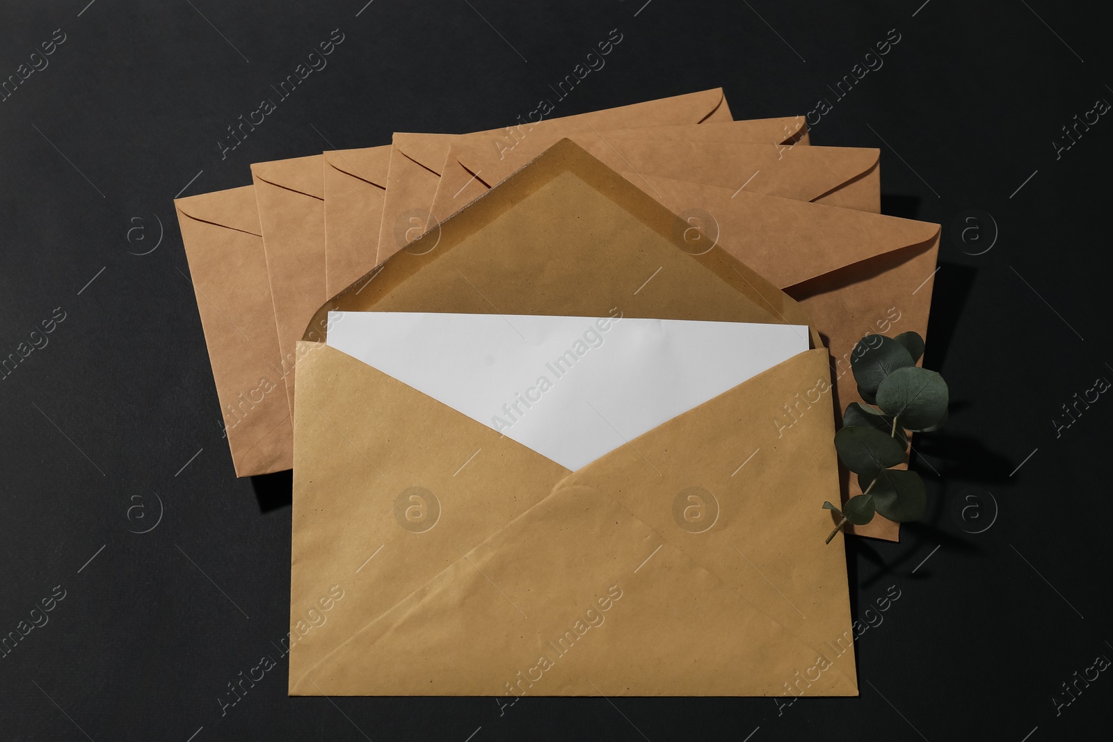 Photo of Kraft paper envelopes with letter and eucalyptus branch on black background, above view. Mockup for design