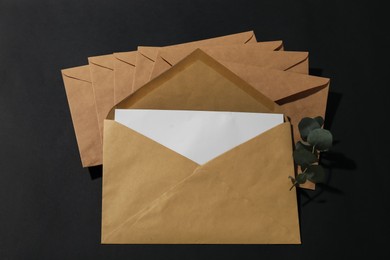 Photo of Kraft paper envelopes with letter and eucalyptus branch on black background, above view. Mockup for design