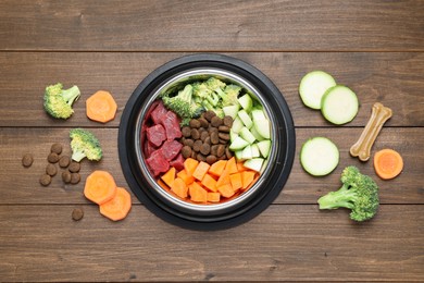 Photo of Dry and natural pet food in feeding bowl among products on wooden table, flat lay