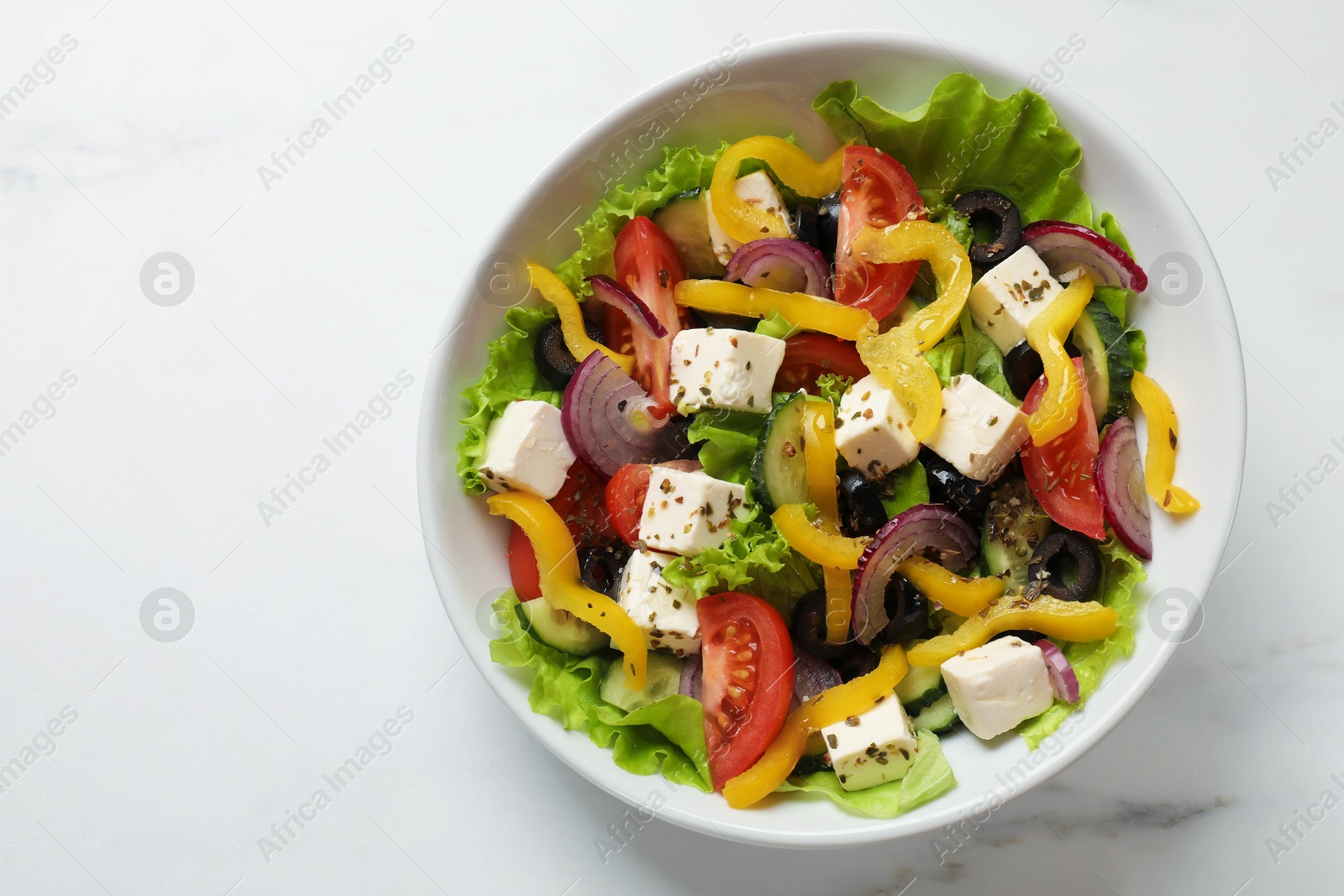 Photo of Delicious fresh Greek salad in bowl on white marble table, top view