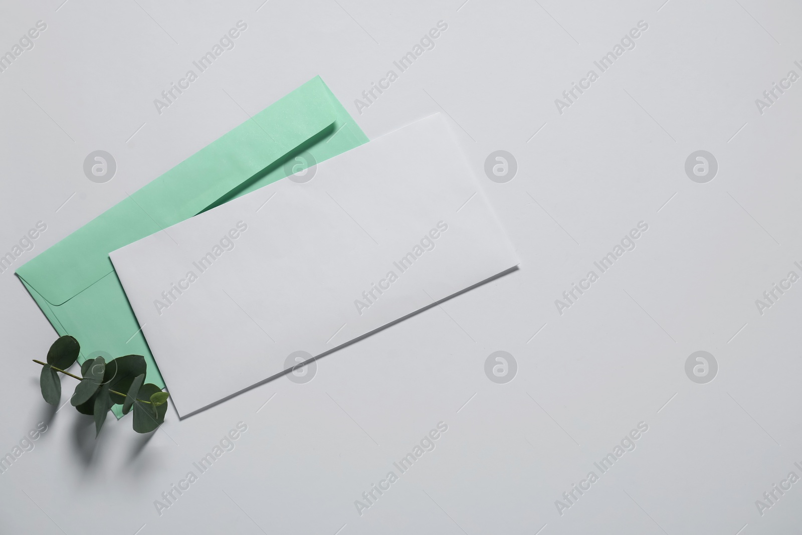 Photo of Paper envelope with letter and eucalyptus branch on white background, flat lay. Mockup for design