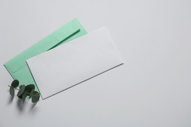 Photo of Paper envelope with letter and eucalyptus branch on white background, flat lay. Mockup for design