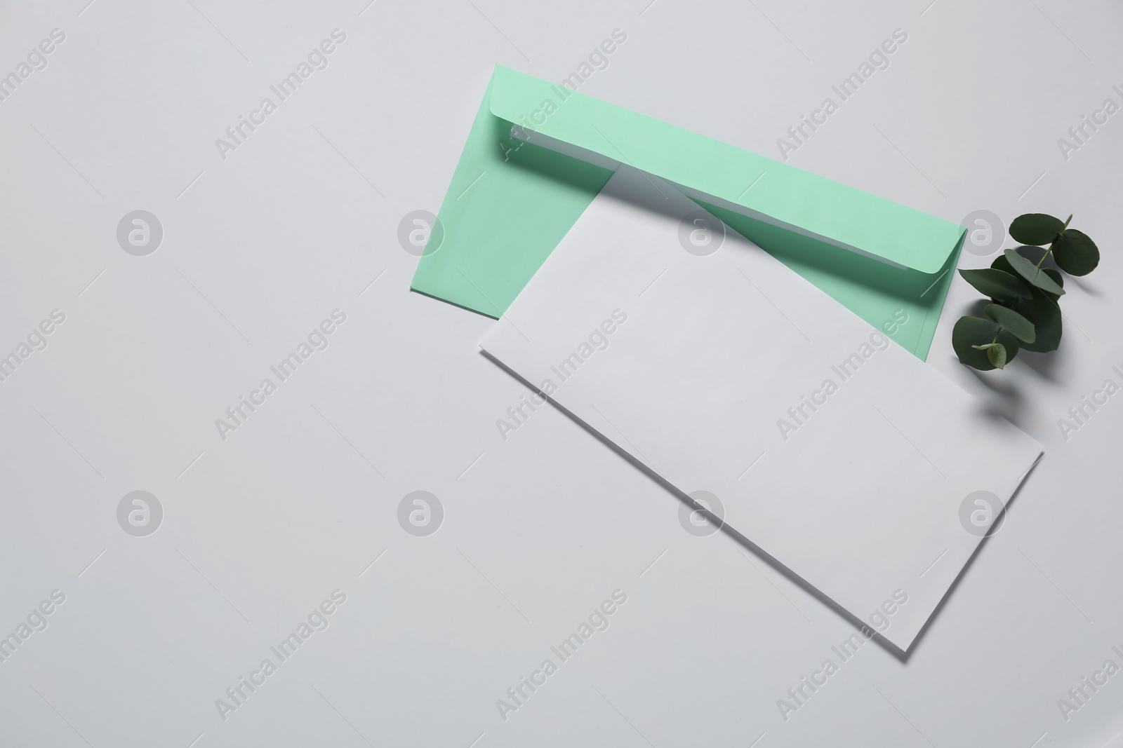 Photo of Paper envelope with letter and eucalyptus branch on white background, flat lay. Mockup for design