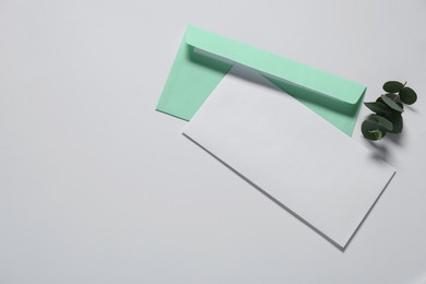 Paper envelope with letter and eucalyptus branch on white background, flat lay. Mockup for design