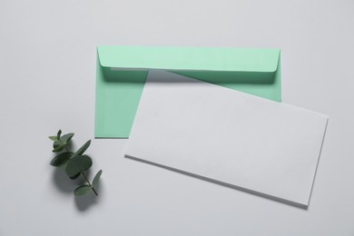 Photo of Paper envelope with letter and eucalyptus branch on white background, flat lay. Mockup for design