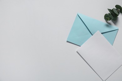 Paper envelope with letter and eucalyptus branch on white background, flat lay. Mockup for design