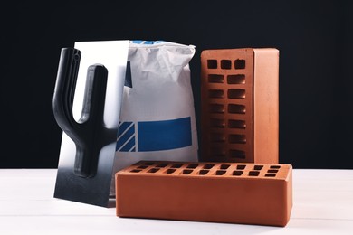 Photo of Bricks, bag of cement and construction tool on white wooden table