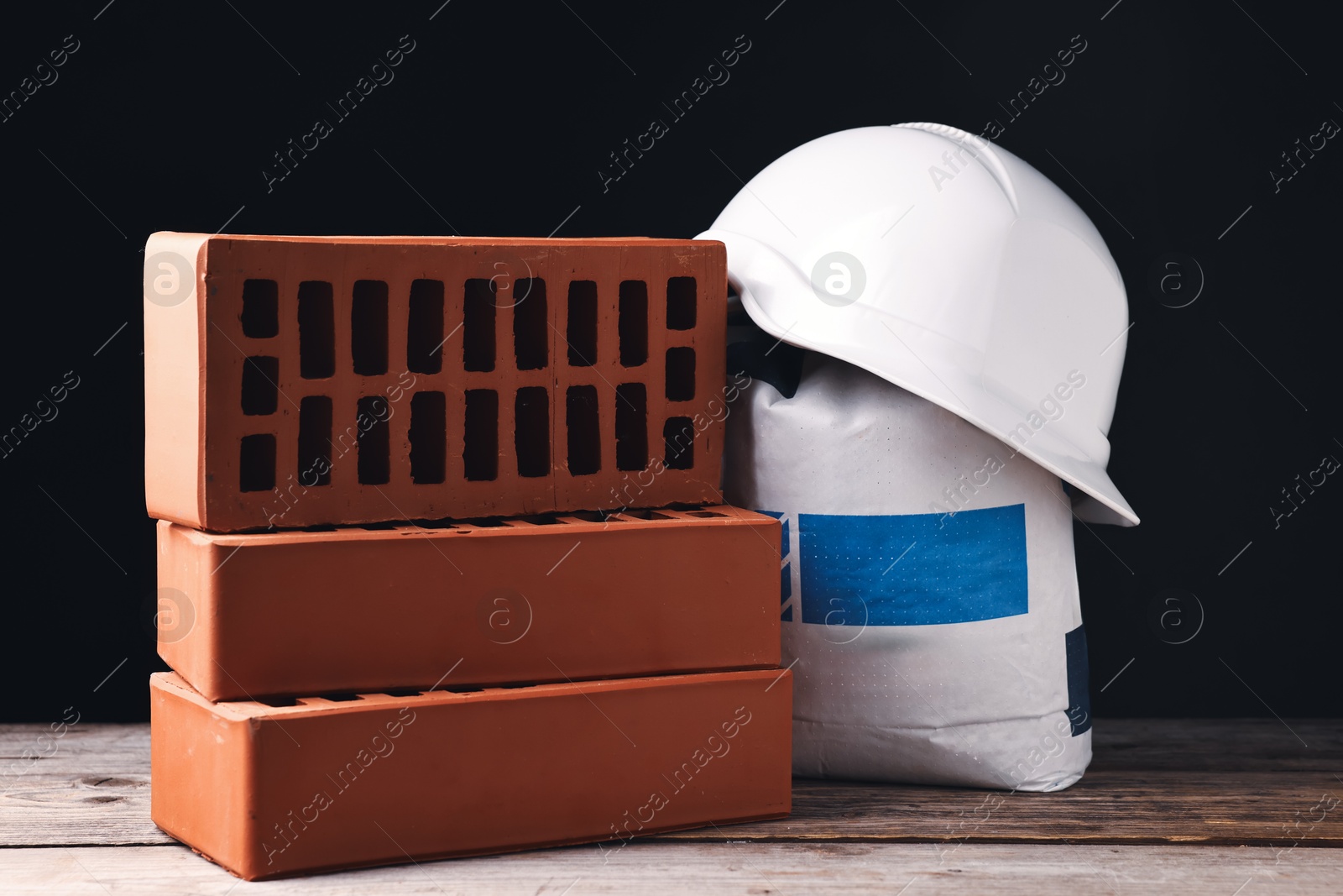 Photo of Bricks, hardhat and bag of cement on wooden table