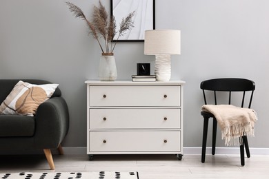 Photo of Dresser, chair and couch near light grey wall in room. Interior design