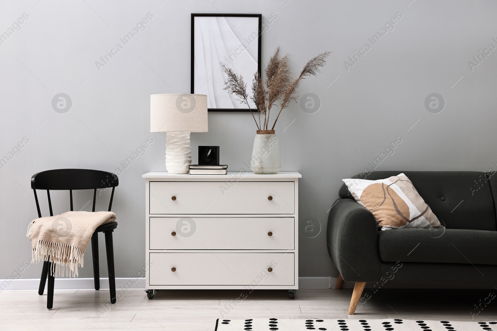 Photo of Dresser, chair and couch near light grey wall in room. Interior design