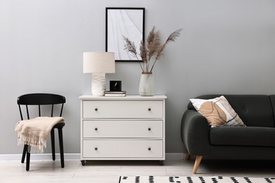 Photo of Dresser, chair and couch near light grey wall in room. Interior design