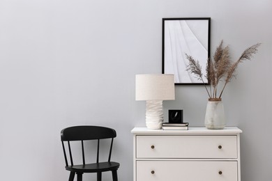 Photo of Dresser and chair near light grey wall in room. Interior design