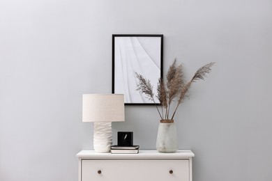 Photo of Console table with lamp, clock, books and vase near light grey wall. Interior design