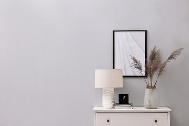 Photo of Console table with lamp, clock, books and vase near light grey wall, space for text. Interior design