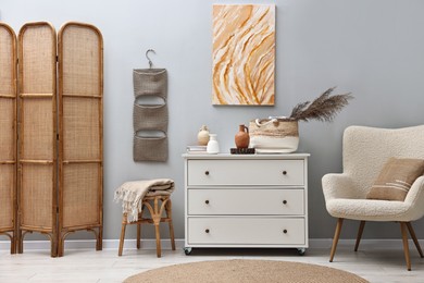 Photo of Dresser and other furniture near light grey wall in room. Interior design