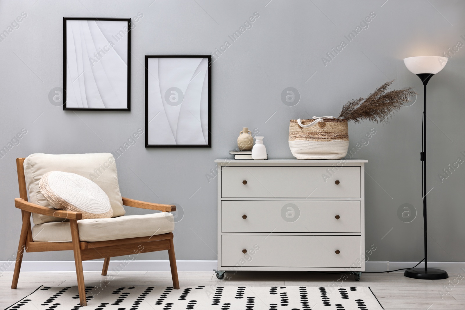 Photo of Dresser, armchair and floor lamp near light grey wall in room. Interior design