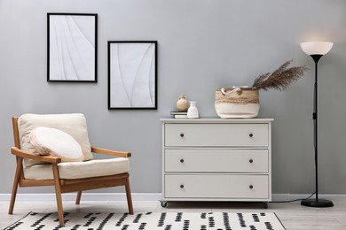 Photo of Dresser, armchair and floor lamp near light grey wall in room. Interior design