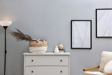 Photo of Dresser, armchair and floor lamp near light grey wall in room. Interior design