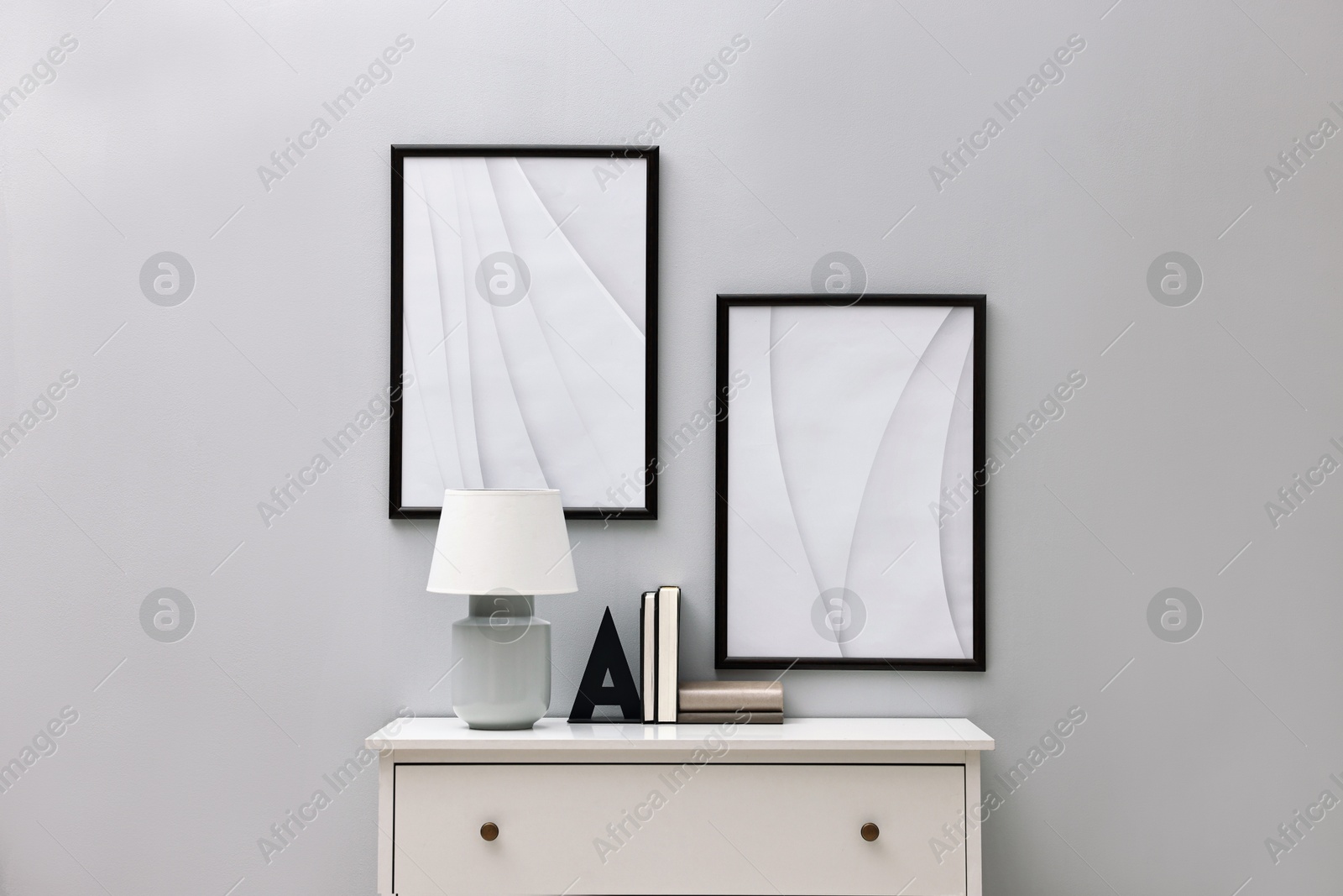 Photo of Console table with lamp and bookend near light grey wall. Interior design