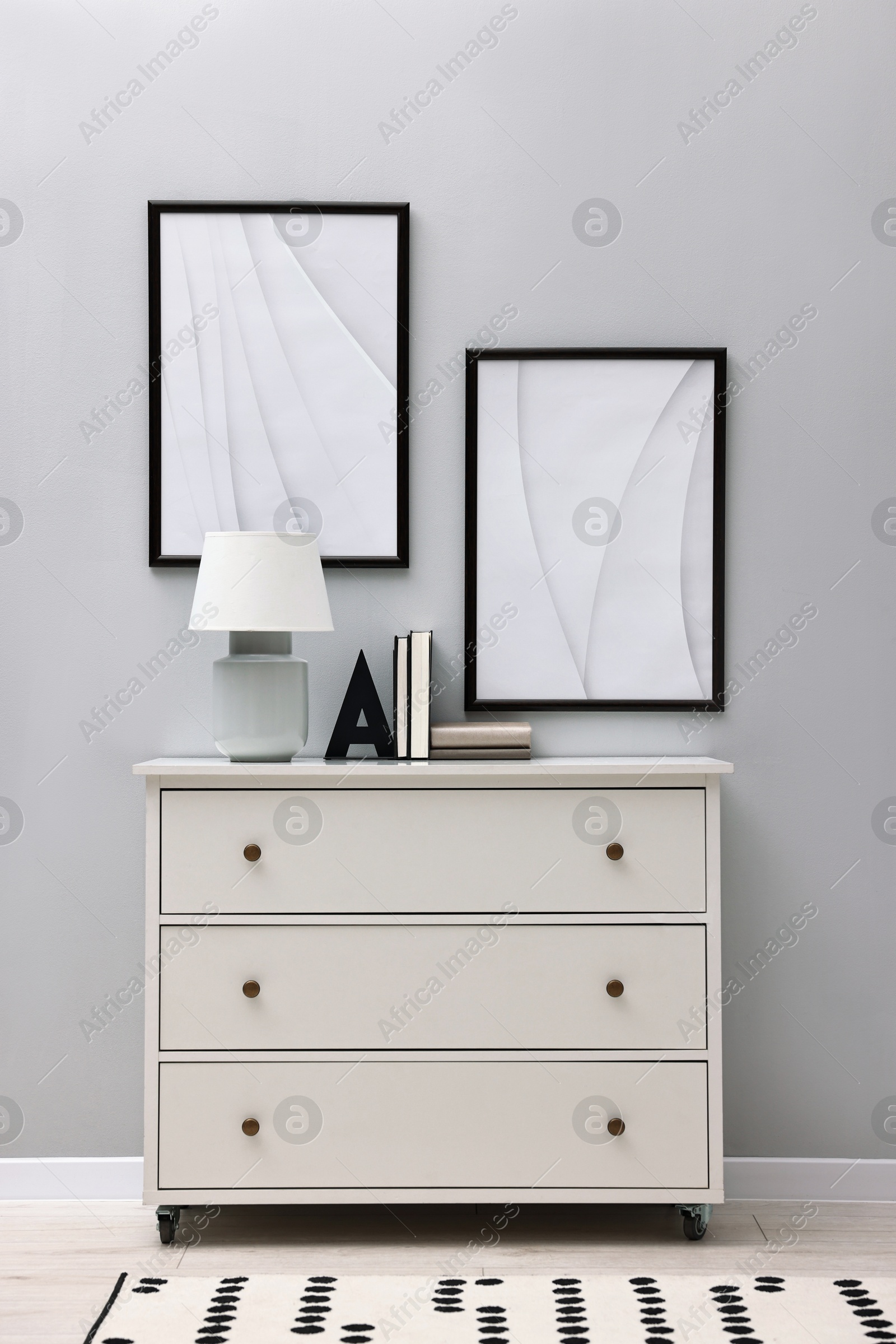 Photo of Dresser with table lamp and bookend near light grey wall in room. Interior design