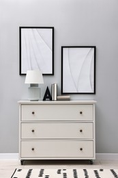 Photo of Dresser with table lamp and bookend near light grey wall in room. Interior design