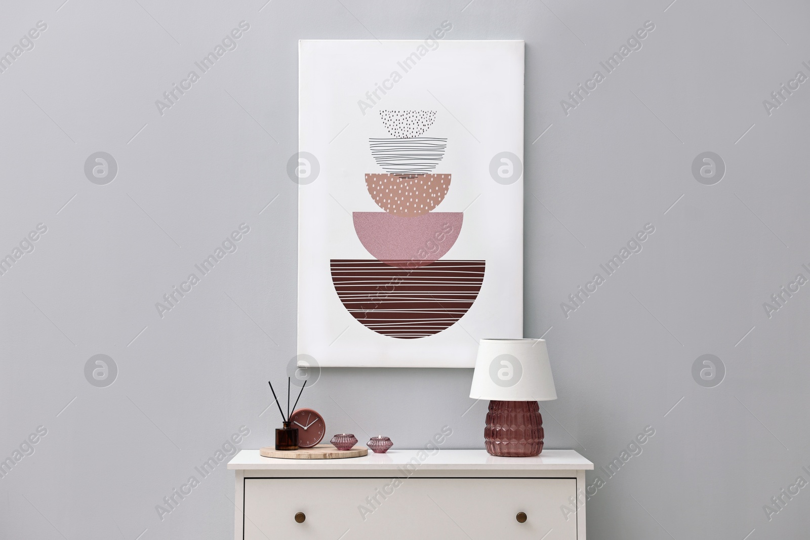 Photo of Console table with lamp, clock reed diffuser and candles near light grey wall. Interior design