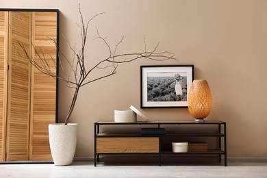 Photo of Console table with lamp and decor near dark beige wall in room. Interior design