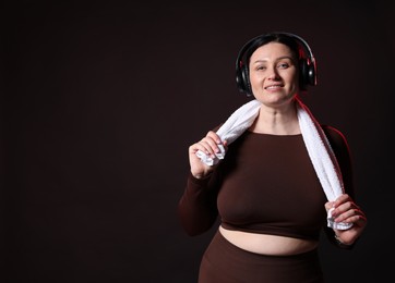 Photo of Plus size woman in gym clothes with headphones and towel on black background, space for text