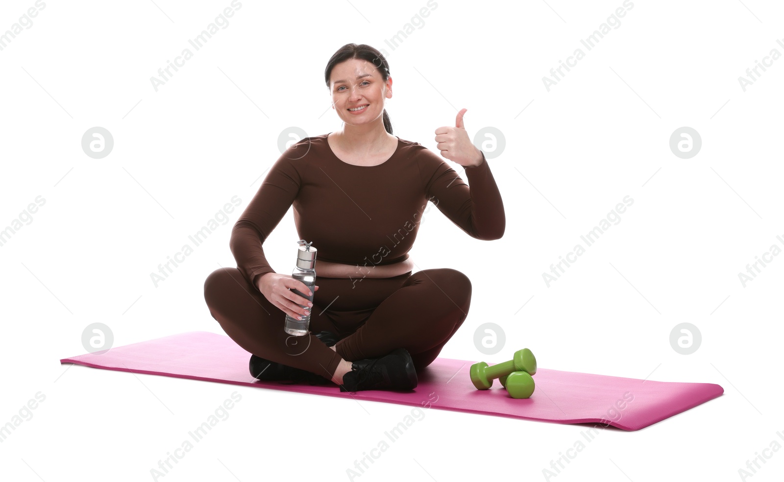 Photo of Plus size woman in gym clothes with water bottle, dumbbells and mat showing thumbs up on white background