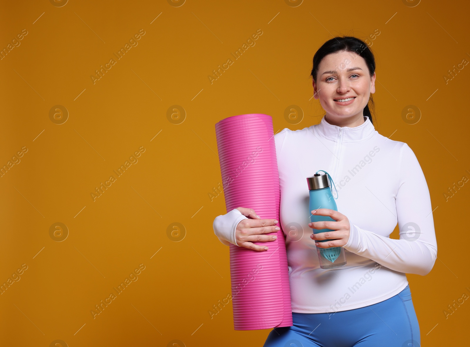 Photo of Plus size woman in gym clothes with water bottle and fitness mat on orange background, space for text