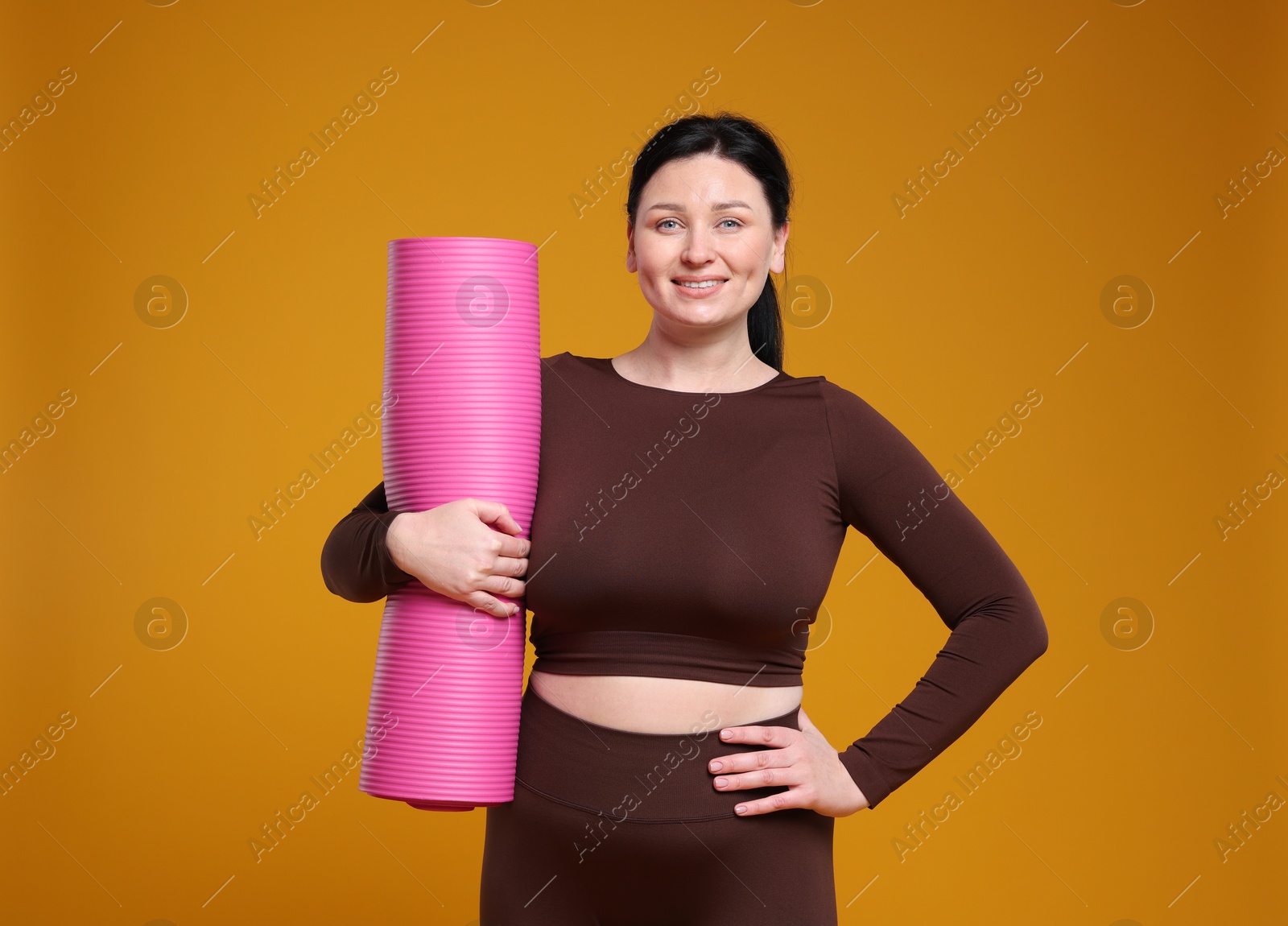 Photo of Plus size woman in gym clothes with fitness mat on orange background