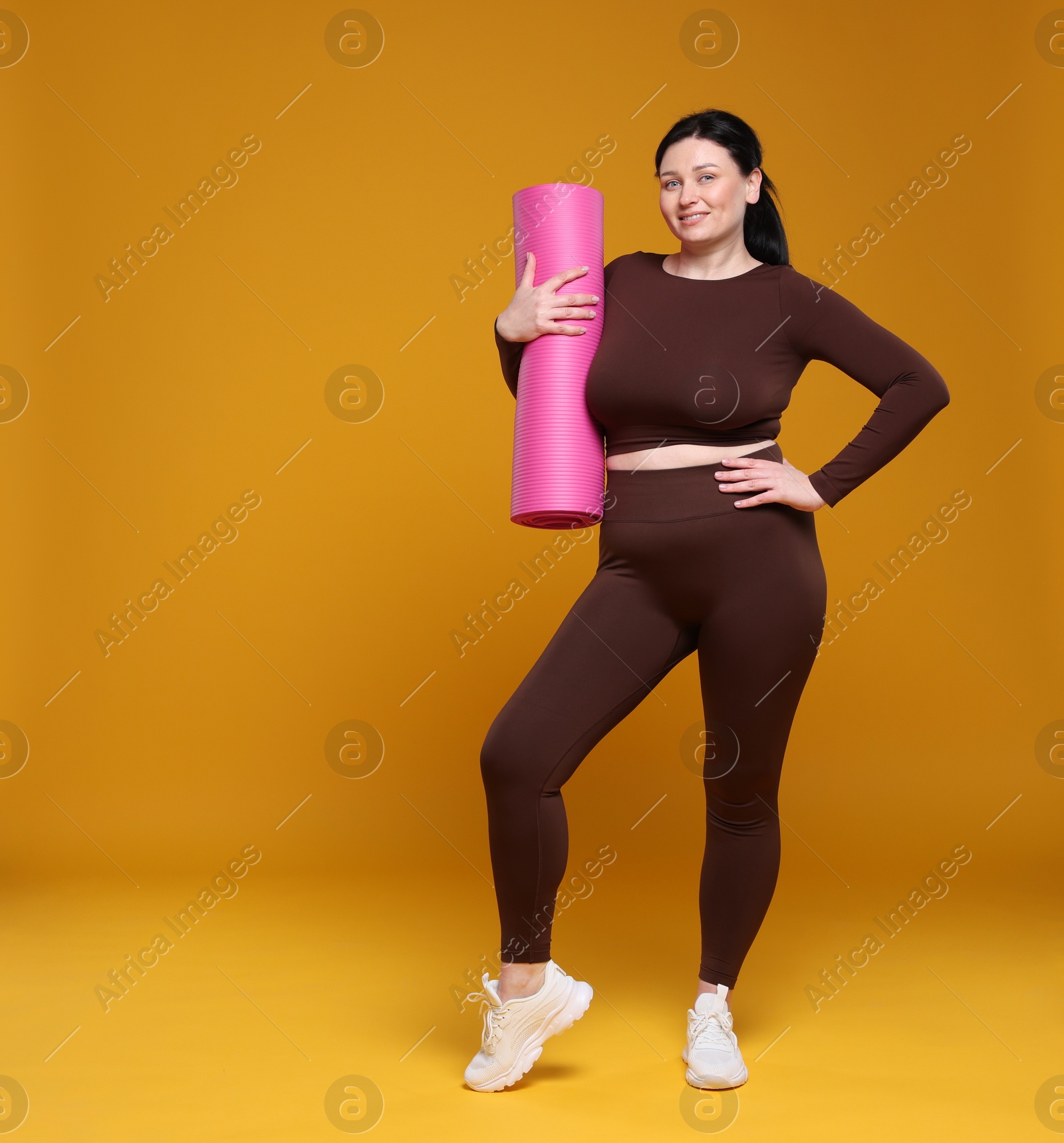 Photo of Plus size woman in gym clothes with fitness mat on orange background, space for text