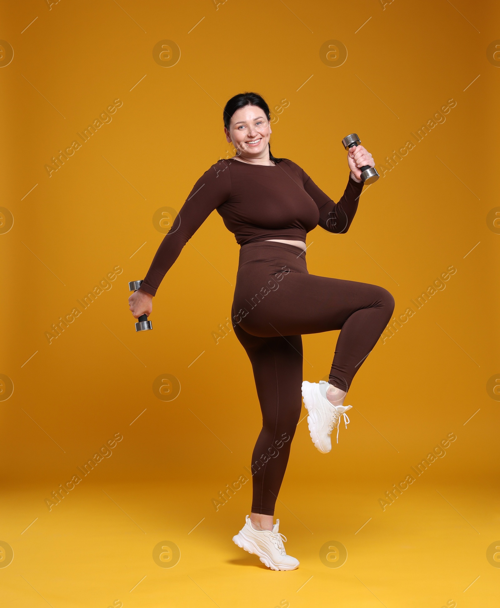 Photo of Plus size woman in gym clothes with dumbbells on orange background