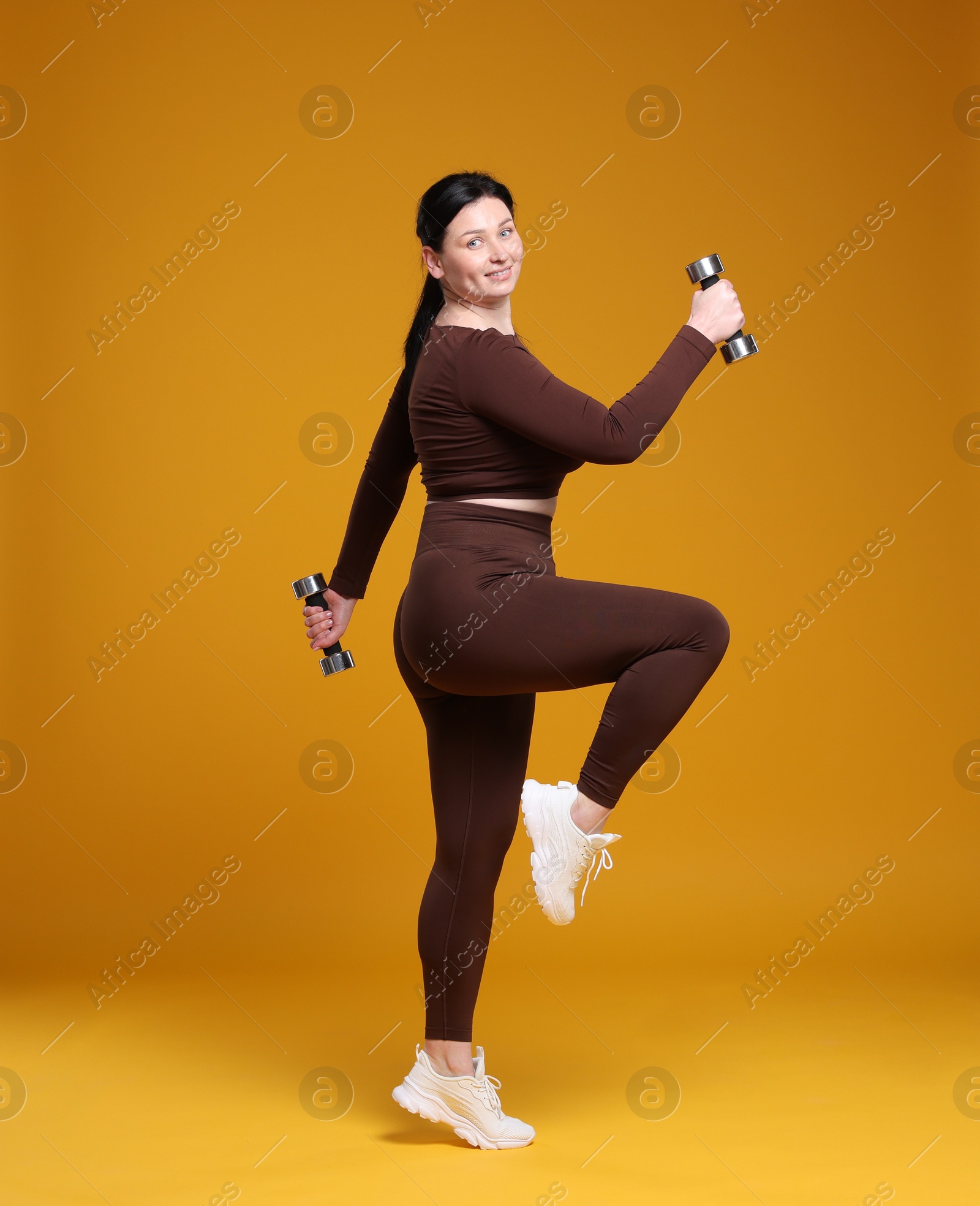 Photo of Plus size woman in gym clothes with dumbbells on orange background