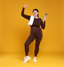 Photo of Plus size woman in gym clothes with water bottle and towel on orange background