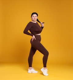 Photo of Plus size woman in gym clothes on orange background