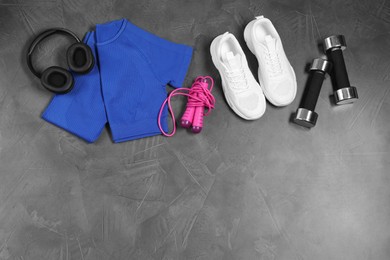 Photo of Stylish sportswear, white sneakers, dumbbells, skipping rope and headphones on grey background, flat lay. Space for text