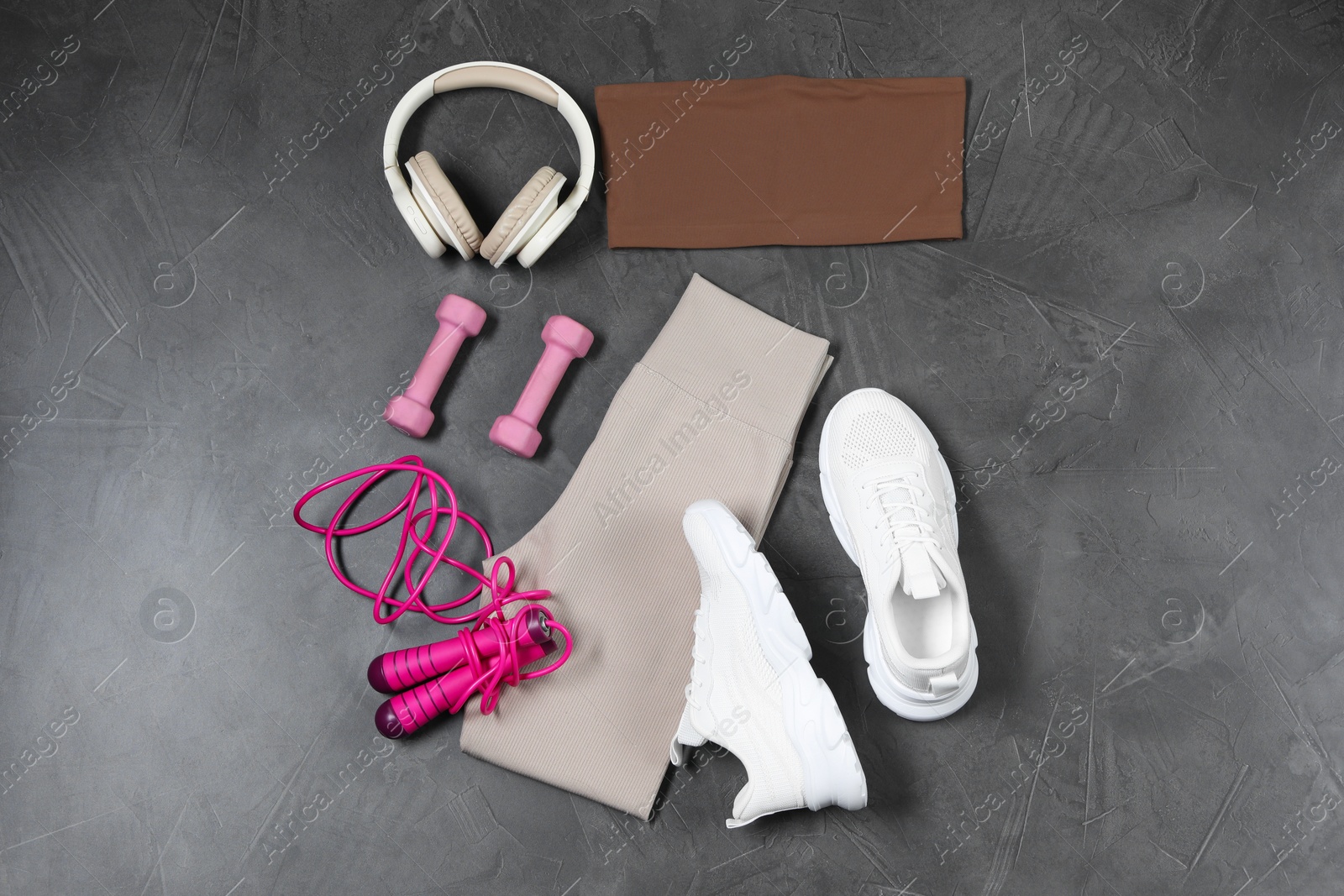 Photo of Stylish sportswear, dumbbells, white sneakers, skipping rope and headphones on grey background, flat lay