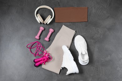 Photo of Stylish sportswear, dumbbells, white sneakers, skipping rope and headphones on grey background, flat lay