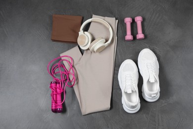 Photo of Stylish sportswear, dumbbells, white sneakers, skipping rope and headphones on grey background, flat lay