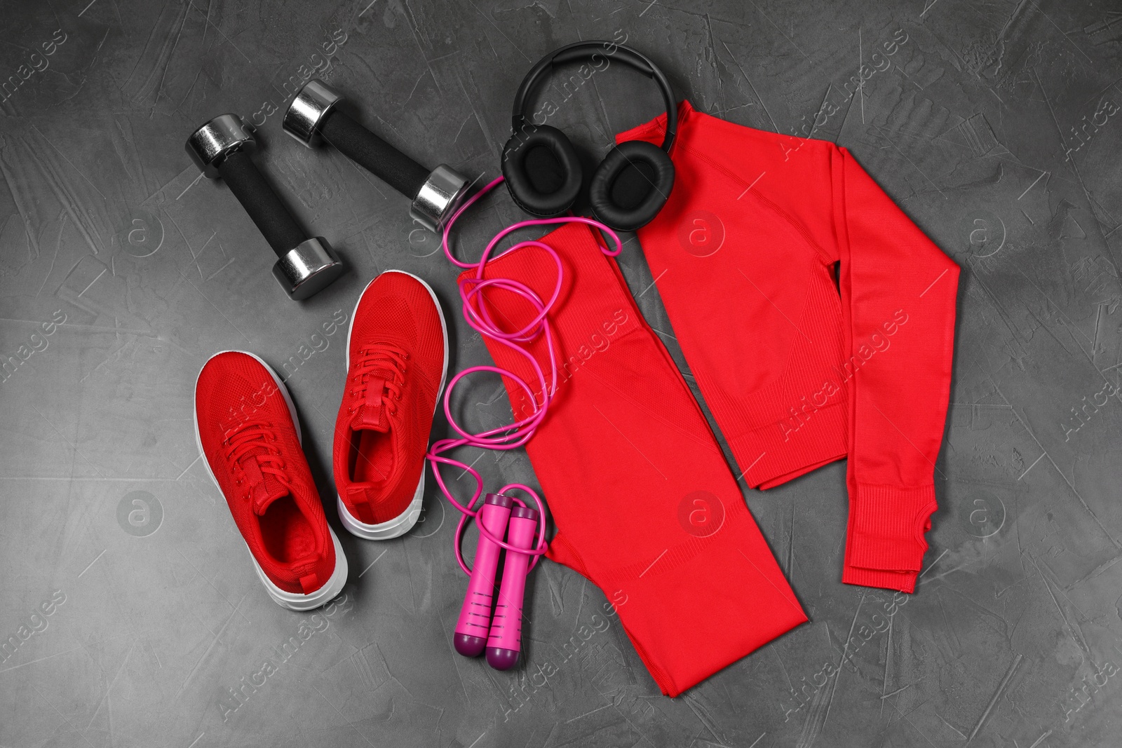 Photo of Stylish sportswear, dumbbells, red sneakers, skipping rope and headphones on grey background, flat lay