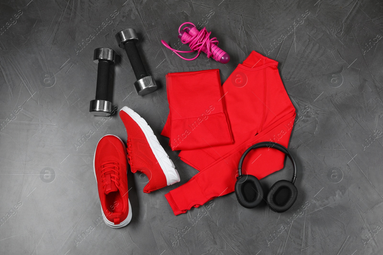 Photo of Stylish sportswear, dumbbells, red sneakers, skipping rope and headphones on grey background, flat lay